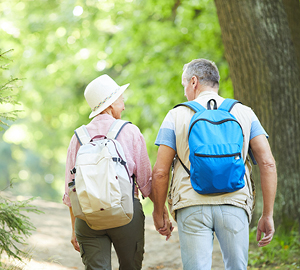 Older couple with back packs on walking on a trail.