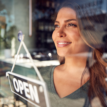 Businesswoman smiling through the window of her shop. An open sign is on the door.