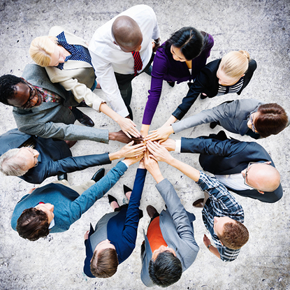 Group of coworkers in a circle stacking their hands together.