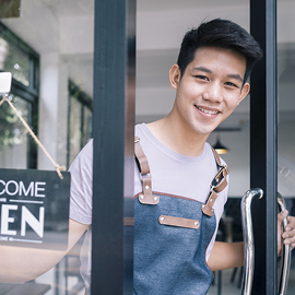 Business owner standing at the door of his store by a welcome/open sign
