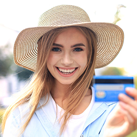 Young woman wearing a straw hat smiling while holding a credit card