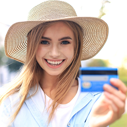 Young girl wearing a straw hat smiling while holding her debit card.