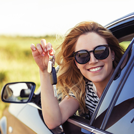 Young woman wearing sunglasses, smiling and holding keys outside of her car